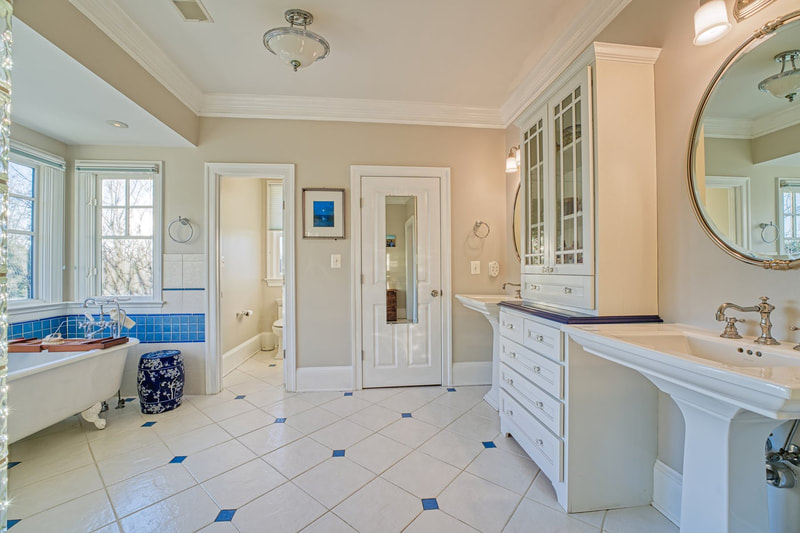 The attached primary bathroom is gorgeous with two sinks separated by a large cabinet with drawers beneath and there is a freestanding claw foot tub with windows and also a shower